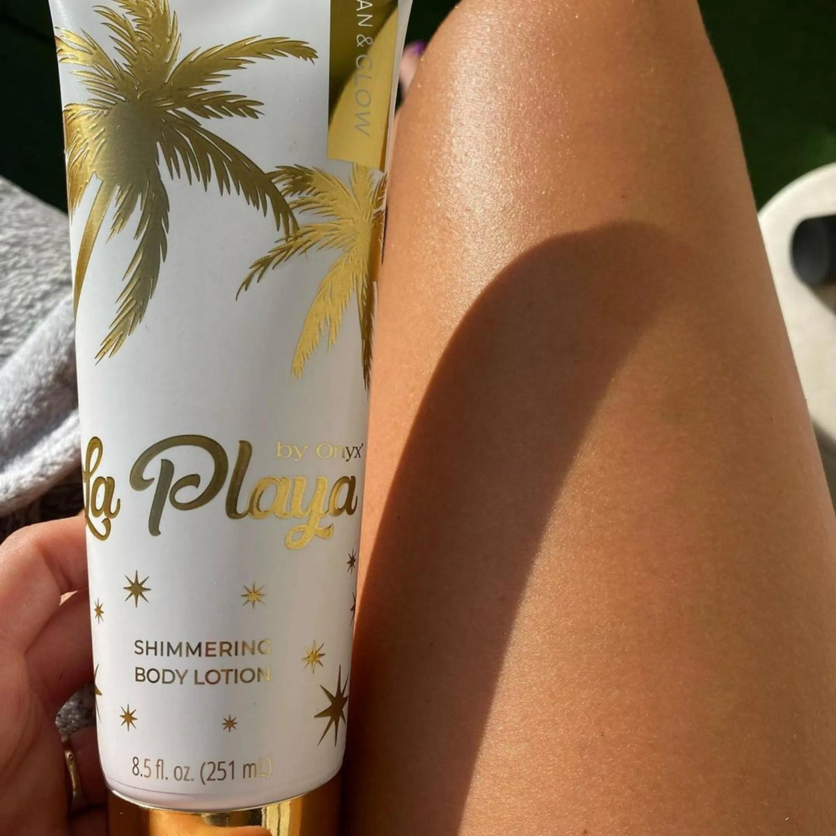 Zbliżenie na kobiecą nogę w słońcu, w dłoni trzymany balsam do ciała Onyx La Playa Tan & Glow, skóra z delikatnym połyskiem po aplikacji balsamu z drobinkami