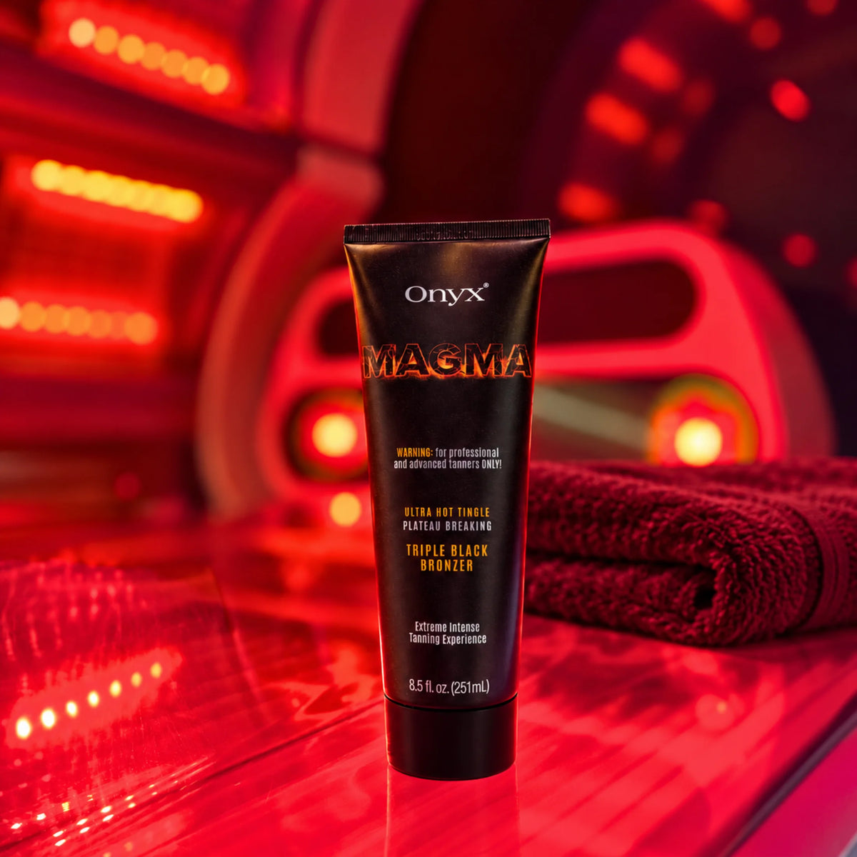 Onyx Magma Tingle stojący wewnątrz czerwono oświetlonego łóżka solaryjnego obok złożonych ręczników. Produkt pokazany w typowym otoczeniu jego zastosowania.