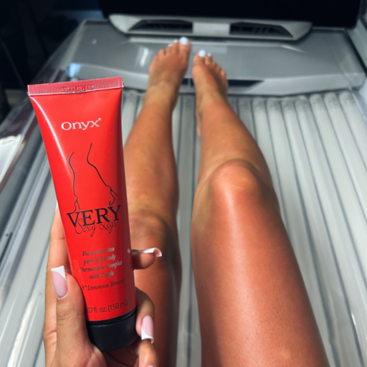 Nogi kobiety w solarium z bronzerem Onyx Very Sexy Legs w dłoni. Balsam z efektem tingle intensyfikuje kolor skóry podczas opalania.