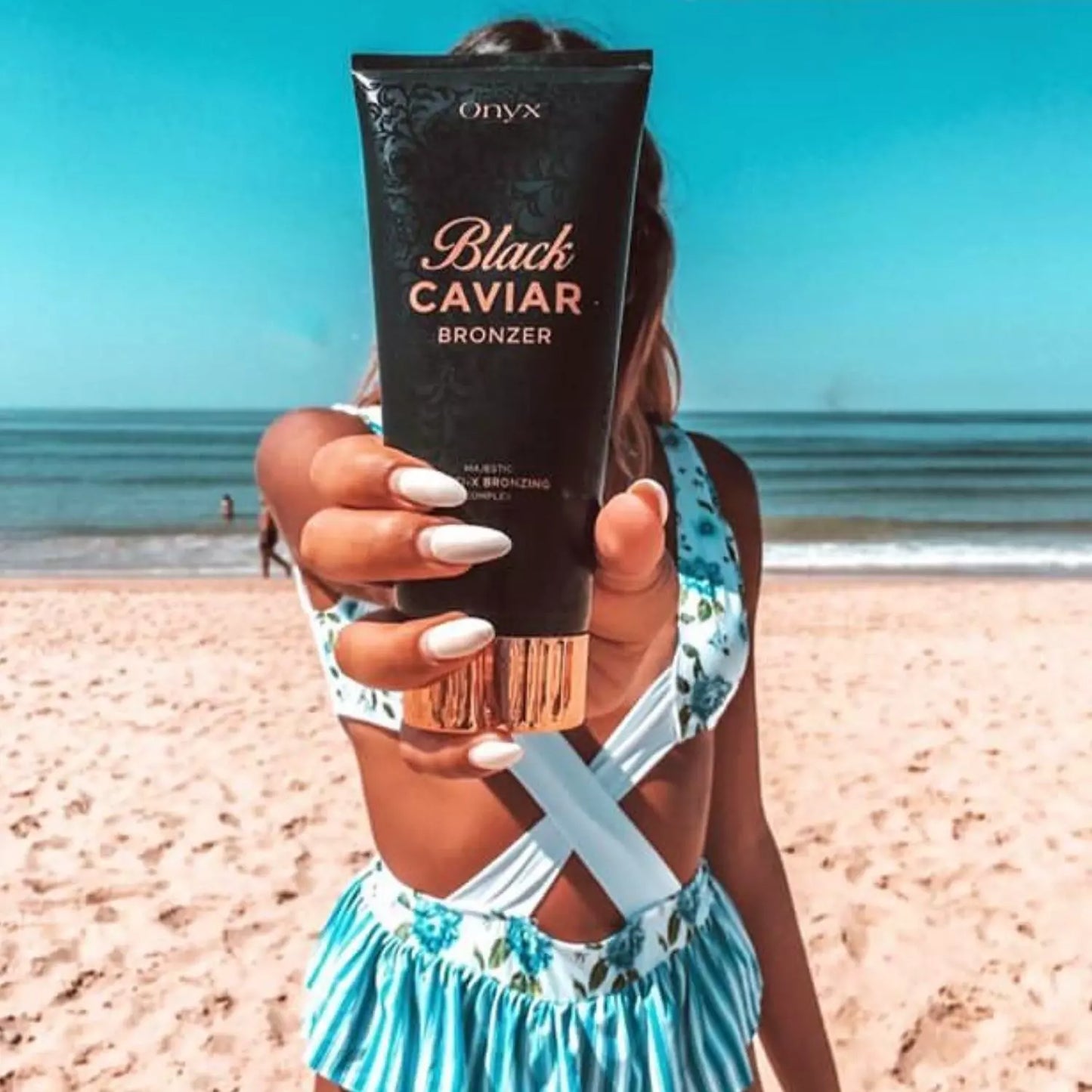 Kobieta na plaży trzyma Onyx Black Caviar Bronzer; bronzer do opalania na słońcu z efektem naturalnej, złocistej opalenizny