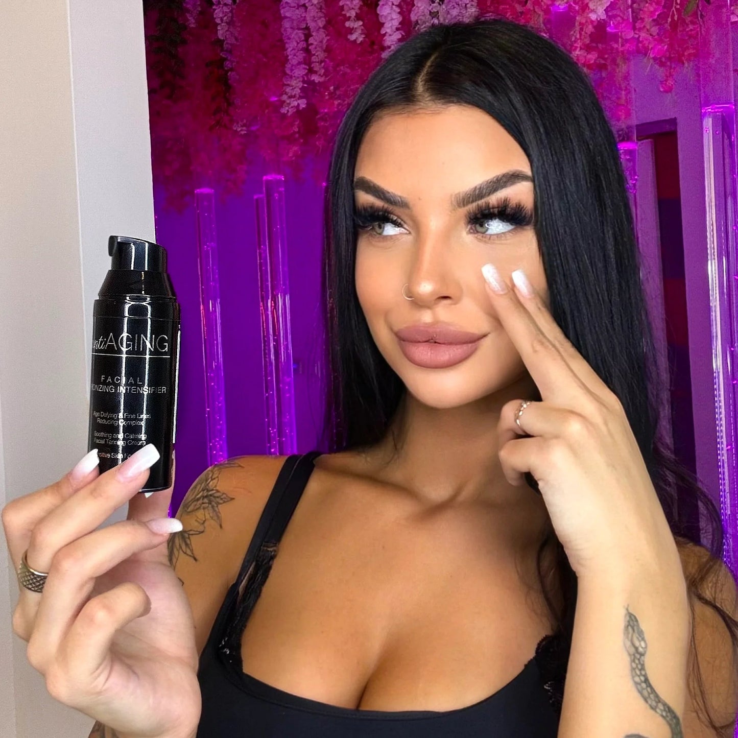 Kobieta w czarnym topie trzyma przy twarzy czarną butelkę kosmetyku Onyx Anti-Aging na tle wnętrza z fioletowym oświetleniem.