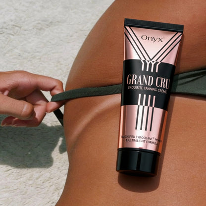 Onyx Grand Cru pokazany przy skórze kobiety na plaży. Zdjęcie prezentuje produkt w outdoorowym kontekście opalania.