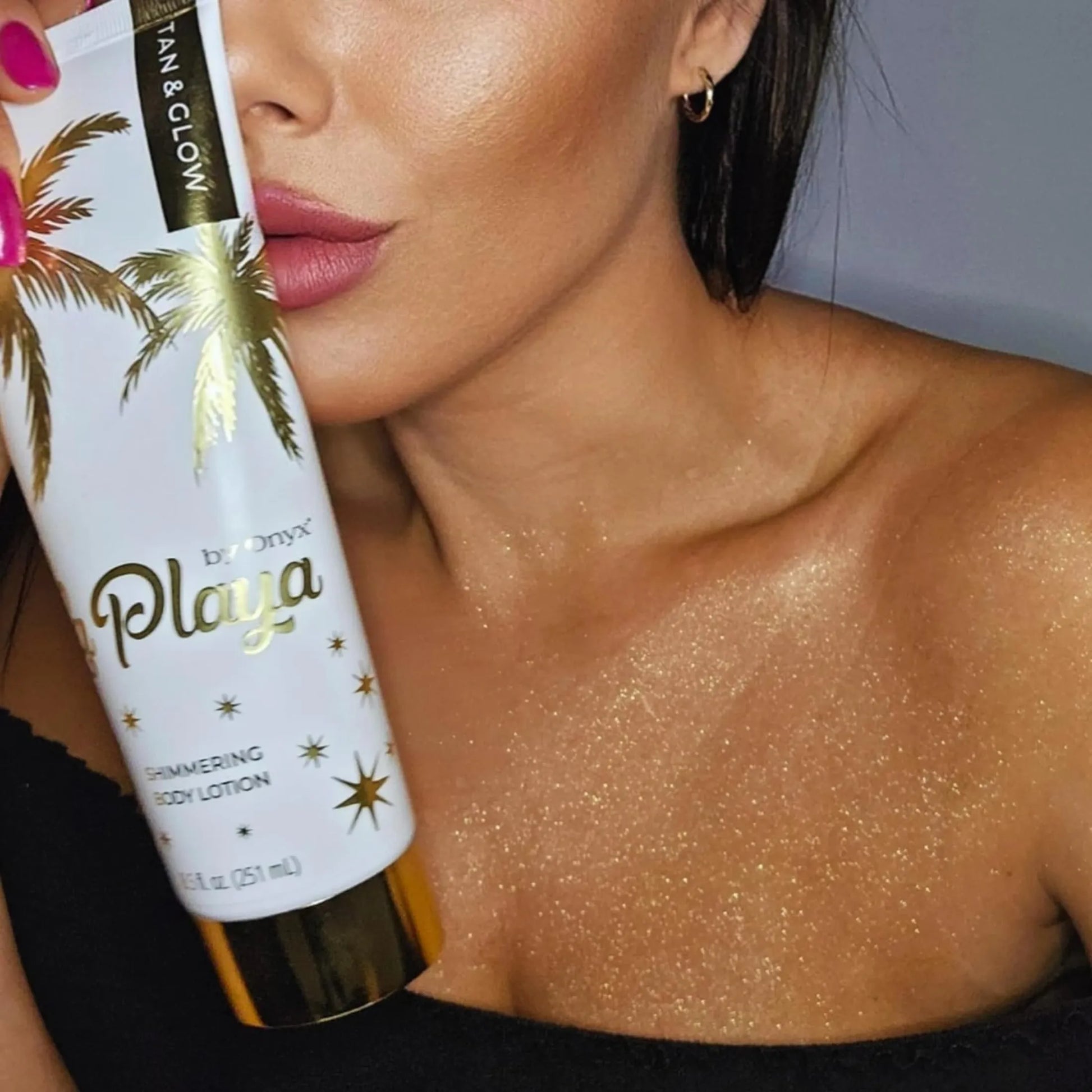 Kobieta trzymająca przy twarzy balsam Onyx La Playa Tan & Glow, jej dekolt i ramiona pokryte są subtelnym złotym blaskiem po zastosowaniu balsamu rozświetlającego