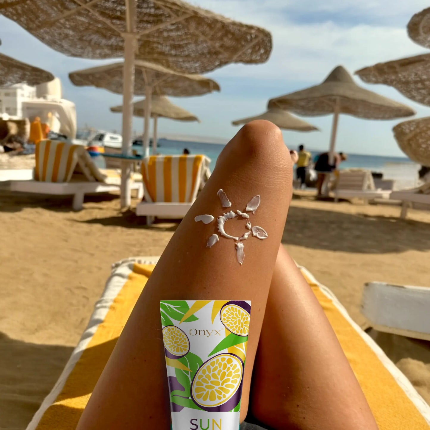 Noga na plaży z rysunkiem słońca i produktem Onyx Suncolada. Naturalny przyspieszacz wspiera złocisty efekt skóry.
