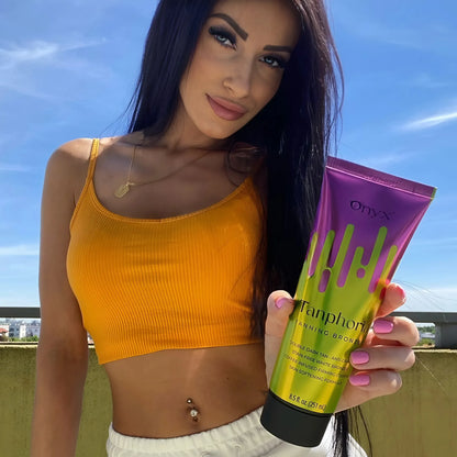 Kobieta z ciemnymi włosami w żółtym topie trzyma balsam do opalania Onyx Tanphoria na tle nieba i słońca