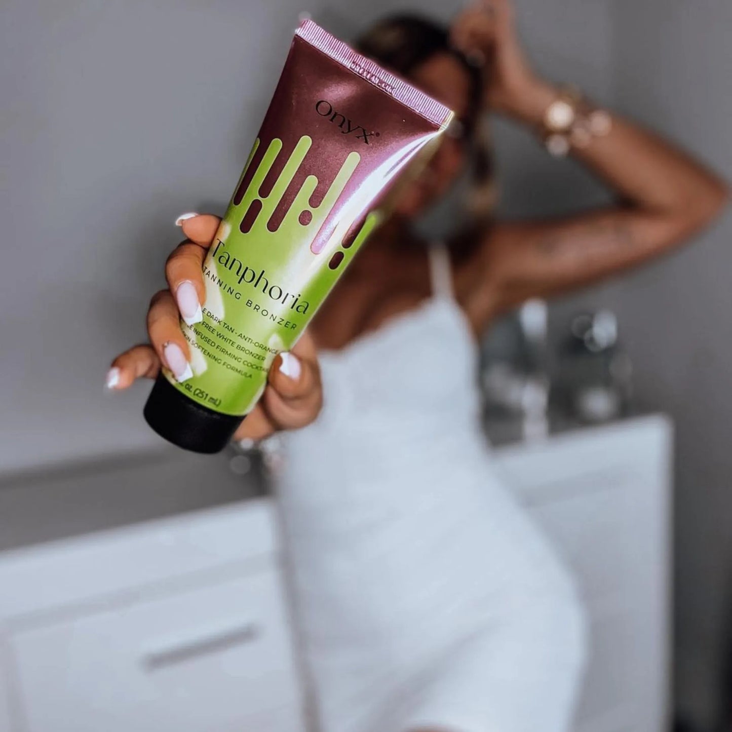 Kobieta w białej sukience trzyma krem do solarium Onyx Tanphoria przed sobą w jasnym wnętrzu