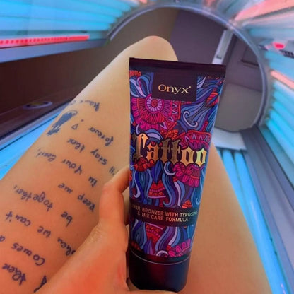 Osoba trzyma tubę balsamu Onyx Tattoo Bronzer nad nogą z tatuażem, siedząc w solarium w różowo-niebieskim świetle lamp, produkt do opalania i podkreślenia kolorów tatuaży