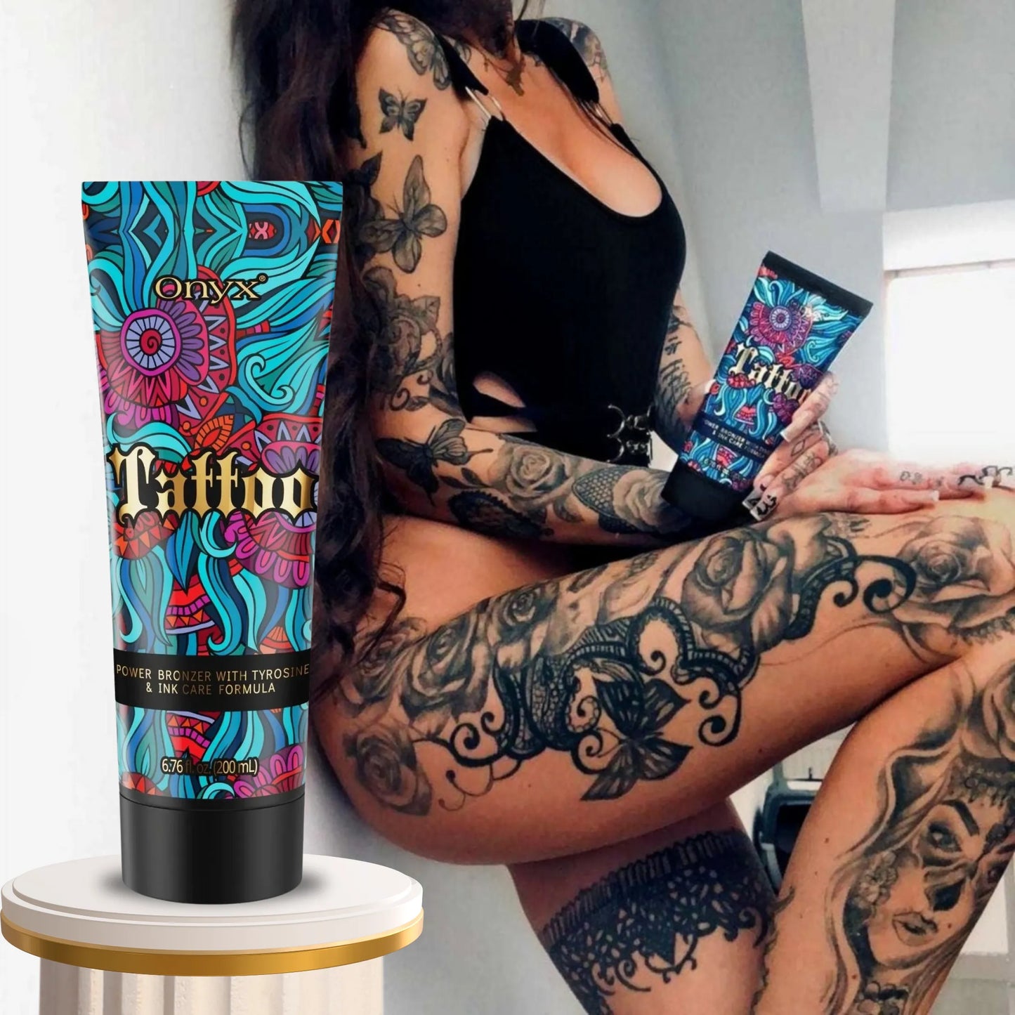 Kobieta z licznymi tatuażami na ciele w czarnym body trzyma balsam Onyx Tattoo Bronzer, pokazując jego działanie na intensywność i blask tatuaży