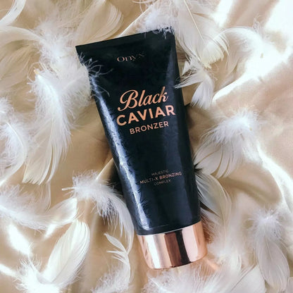 Onyx Black Caviar Bronzer położony na złotej satynie z białymi piórami; elegancki bronzer do opalania zapewniający luksusowy efekt skóry muśniętej słońcem